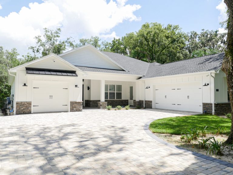 Modern white single-story home with three-car garage, solar panels, and curved driveway surrounded by landscaping